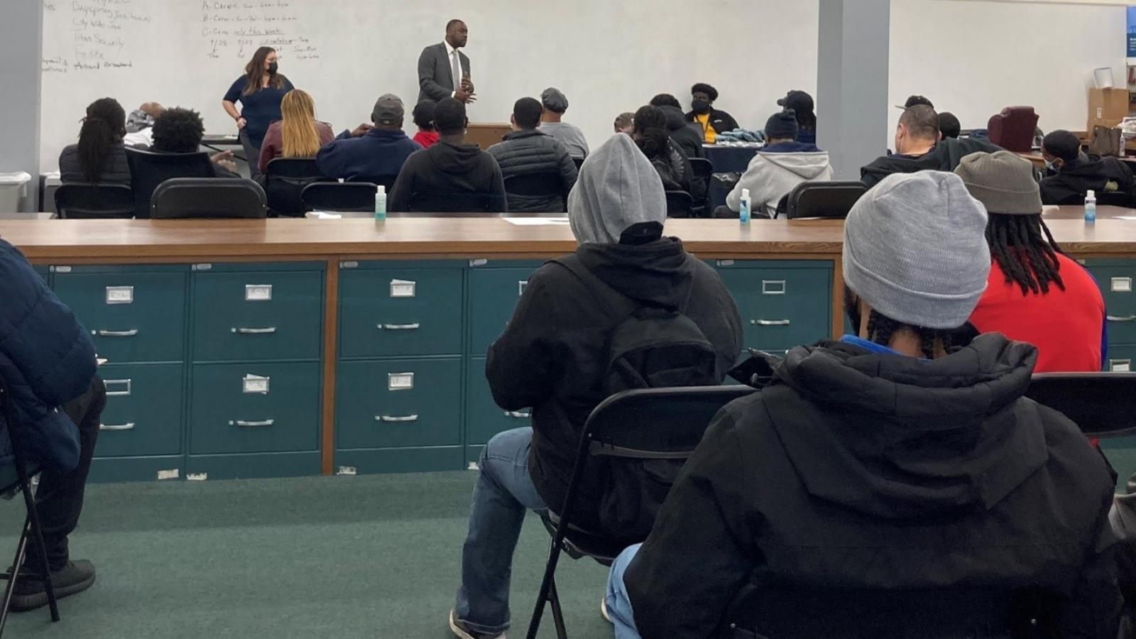 A classroom of high school students sit in a classroom while representatives from the Cook County Public Defender's Office speak at the front of the room. 